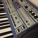 Detailní pohled na ovládací panel modrého klaviru s bílými a černými klávesami. Na panelu jsou viditelné sekce s nápisy SAMPLER PLAYER, ARPEGGIO, PAR…