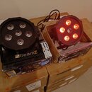 Dvě černé LED par lampy s šesti světelnými zdroji, z nichž jedna svítí červeně. Na základně levé lampy je bílý nápis beamZ. Pod přístroji jsou karton…