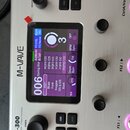 Stříbrný efektový procesor značky M-WAVE. Zařízení má digitální displej s fialovým rozhraním, tři stoupací spínače s růžovým podsvícením a dva černé…