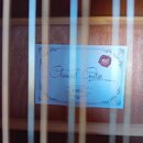 Fotografie zachycuje vnitřek akustické kytary s viditelným štítkem na lícové desce. Na modrém štítku je nápis Classical Guitar, pod kterým jsou text…