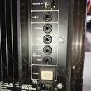 Detail zadní strany černého elektronického zařízení s ovládacími prvky. Jsou zde nápisy VOLUME, LIMIT, LINE IN, IN (LEFT/MO, RIGHT), OUT MID/HIGH (LE…