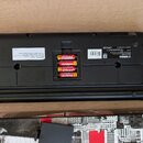 Zadní strana černého plastového hudebního nástroje značky YAMAHA. V otevřeném prostoru pro baterie jsou vloženy čtyři žluté baterie značky KODAK. Na…