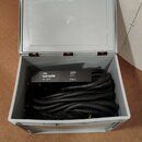 Šedý plastový přepravní kufr s otevřeným víkem, v němž jsou svinuté černé audio kabely. Na jednom z kabelů je viditelný černý štítek s bílým nápisem…
