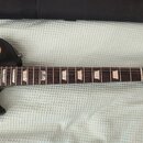 Černá elektrická kytara s hnědým hmatníkem a trapezoidními vložkami. Na hlavě je bílý nápis „Les Paul Model“ a logo „Gibson“. Tělo má hnědý plastový…