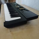 Černý elektronický klavír s bílými a černými klávesami. Na horním panelu jsou umístěny ovládací tlačítka, z nichž část je žlutá. V horní části je vid…
