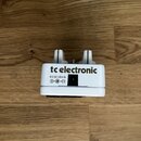 Bílá kytarový efekt s nápisem tc electronic. Na spodní straně je uveden text 9 V DC 40 mA a schéma polarity napájení. Zařízení vykazuje mírné znečišt…