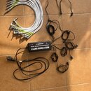 Na fotografii je černý napájecí adaptér s nápisem MULTI POWER SUPPLY, SEPARATE ISOLATED 8X DC10V / 100mA a značkou SMBCKALLIEFFECTS. K adaptéru patří…