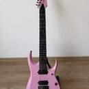 Růžová elektrická kytara s černým hmatníkem a černým hardwarem, umístěná na stojanu. Na hlavě je viditelné logo "Cort". Nástroj má dva humbuckery a f…