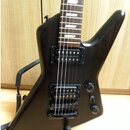 Černá elektrická kytara s hrotovitým tvarem korpusu a tmavým hmatníkem s bílými vložkami. Nástroj je vybaven dvěma černými humbuckery, dvěma potencio…
