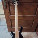 Zadní pohled na elektrickou basovou kytaru s černým trupem a světlým dřevěným hnedkem. Na hlavě nástroje je viditelné logo "Squier". Povrch instrumen…
