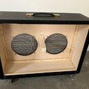 Černý kytarový reproduktorový box s otevřeným předním panelem. Uvnitř je vidět světlé dřevěné provedení a dva reproduktory s černými ochrannými mřížk…
