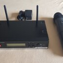 Černý bezdrátový přijímač s dvěma anténami a doprovodný černý bezdrátový mikrofon. Na předním panelu přijímače je nápis XS WIRELESS TRUE DIVERSITY RE…