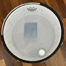 Fotografie znázorňuje bílý buben s napnutou membránou. Na horní části membrány je černé logo REMO a pod ním nápis SILENTSTROKE MADE IN U.S.A. V centr…