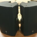 Dva černé akustické reproduktory s kovovou mřížkou v přední části. V dolní části každého reproduktoru je umístěno malé kulaté logo s vyobrazením zvíř…