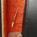 Na oranžové plišové výstýlce v kufru leží kovový imbusový klíč s bílou plastovou rukojetí. Pod ním se nachází průhledný plastový obal s několika malý…