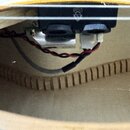 Detail vnitřku akustické kytary s instalovaným elektronickým předzesilovačem. Na černém plastovém krytu je viditelné logo GUILD s písmenem G. Jsou zd…