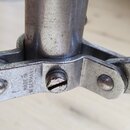 Detail kovového spojení nohy stojanu s centrální trubkou. Na kovovém prvku je vyražen nápis MADE IN W GERMANY. Povrch kovu vykazuje známky opotřebení…