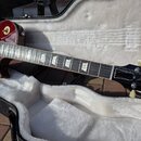 Elektrická kytara s tělem v červeně-žlutém sunburst provedení, položená v otevřeném černém kufru s bílou výplní. Na hlavě kytary je bílé logo Gibson…