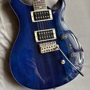 Modrá elektrická kytara s prosvítající strukturou dřeva a bílým lemováním. Nástroj má dva humbuckery, jeden ovládací knoflík hlasitosti a jeden tónu,…