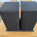 Dva černé regálové reproduktory s textilními maskovacími mřížkami. Na horní hraně mřížek je nápis Bowers & Wilkins, v dolní části mřížek se nachází l…