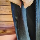 Detailní pohled do vnitřku černého textilního obalu nebo pouzdra. Ruka drží a odtahuje vrstvu měkké, černé vnitřní výplně. Na pravé straně je viditel…