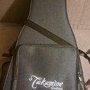 Šedý polstrovaný obal na kytaru s přivázaným popruhem. Na přední kapsi je bílý nápis Takamine Guitars. Povrch textilie vypadá čistě a bez viditelného…