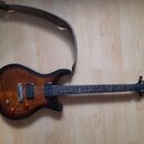Elektrická kytara s prohnutým korpusem v tmavě hnědém sunburst provedení s viditnou sletovanou strukturou dřeva. Nástroj má dva humbuckery, jeden ovl…