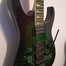 Elektrická kytara s tmavě zeleným průsvitným lakem a viditelnou strukturou dřeva na těle. Nástroj má dva humbuckery, tremolo mechanismus s páčkou a s…