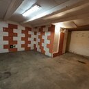 Fotografie znázorňuje prázdnou místnost s betonovou podlahou a bílým stropem s trámovými prvky. Stěny jsou v červenobílé kostkované kombinaci, pravá…
