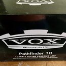 Černý papírový karton s bílými nápisy. Uprostřed je velké logo VOX a pod ním text AMPLIFICATION LTD. Dole je uveden název modelu Pathfinder 10 a popi…