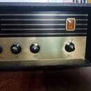 Černý audio zesilovač s kovovým předním panelem v zlatavé barvě. Na horní části je částečně viditelný nápis 35 a oranžová kontrolka. Panel obsahuje č…