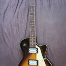 Elektrická kytara s trupem v tmavě hnědé a žluté barvě (sunburst) a bílým pickguardem. Na hlavě hmatníku je nápis Samick a pod ním logo ve tvaru štít…