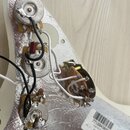 Fotografie zachycuje elektroniku elektrokitary namontovanou na bílém plastovém krytu s hliníkovým stíněním. Jsou vidět tři potenciometry a jeden přep…