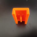 Oranžový plastový držák nebo podstavec s dutým vnitřkem a středovým výstupkem. Předmět vykazuje typickou texturu 3D tisku s viditelnými vrstvami. Žád…