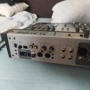 Stříbrný audio rozhraní s černými detaily. Na horním panelu je nápis M-AUDIO a PROJECTMIX I/O. Zadní panel obsahuje různé konektory s popisky ADAT, S…