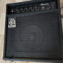 Černý basový kombozesilovač s texturovaným povrchem a černou přední síťovkou. Na horním ovládacím panelu je nápis Ampeg BA-108 a ovládací prvky s pop…