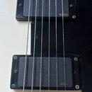 Detail elektrické kytary s bílým tělem a černým pickguardem. Na těle jsou dva černé snímače, z nichž oba mají v pravém dolním rohu zlatý nápis EMG. P…
