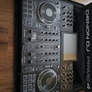 Černý DJ kontrolér Denon DJ Prime 4 umístěný v transportním kufru. Na přístroji jsou vidět dvěsté jog-kola, fadery, knoflíky a displej. Na horní část…