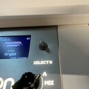 Detailní pohled na ovládací panel bílého elektronického nástroje. Je zde vidět displej s nápisy „Chamberlin“, „M1“, „Organ“ a „<MODE CHANGE>“. Vedle…