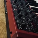 Červený syntetizátor s černými ovládacími knoflíky a klávesami. Na panelu jsou viditelné nápisy VOICE MODE, UNISON, MASTER LEVEL, MIDI, VELOCITY, MOR…