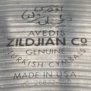 Detailní záběr na povrch kovového činely s koncentrickými rýhami. Jsou zde nápisy: „AVEDIS ZILDJIAN Co“, „GENUINE TURKISH CYMBALS“ a „MADE IN USA“. V…