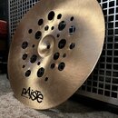 Kruhový mosazný činel s otvory v horní části. Na povrchu je černý nápis paiste a pod ním menší text Made in Switzerland. Povrch vykazuje jemné škrába…