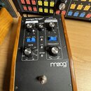Černý efektový pedál v dřevěném šasi s nápisem moogerfooger RING MODULATOR MODULATOR. Zařízení obsahuje čtyři otočné ovladače, dva přepínače a jeden…
