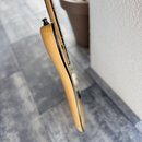 Detailní pohled na hranu těla elektrické kytary v přírodní dřevěné barvě. Je vidět část hředu a černý knoflík u horní části těla. Povrch nástroje vyp…