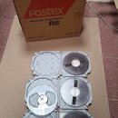 Kartonová krabice s nápisy „FOSTEX R8“, „FRAGILE / HANDLE WITH CARE“ a „Recorder/Reproducer R8“. Na krabici je červený pruh s logem „Fostex“ a texty…