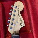 Hlava elektrické kytary z přírodního světlého dřeva s nápisem Fender® STRATOCASTER. V horní části je malý nápis Custom Shop. Na hlavě jsou umístěny š…
