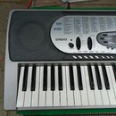 Stříbrošedý elektronický klavír značky CASIO. Na horním panelu jsou viditelné nápisy 100 RHYTHMS a 137 TONES spolu s rozsáhlým seznamem rytmů a zvuků…