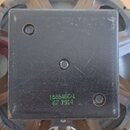 Fotografie zachycuje zadní část reproduktoru s černým, čtvercovým magnetem. Na povrchu magnetu je zelený nápis 15854BC-1 a pod ním číslo 67.7914. Pov…