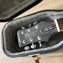 Černá kytara v otevřeném kufru s šedým vnitřním polstrováním. Na hlavě kytary jsou zlaté nápisy Epiphone, Les Paul MODEL a Les Paul STANDARD. Povrch…