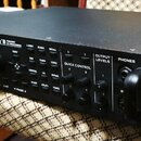 Černý rackový procesor s nápisem Axe-Fx II PREAMP FX PROCESSOR a logem FRACTAL AUDIO SYSTEMS. Přední panel obsahuje displej, ovládací knoflíky, tlačí…